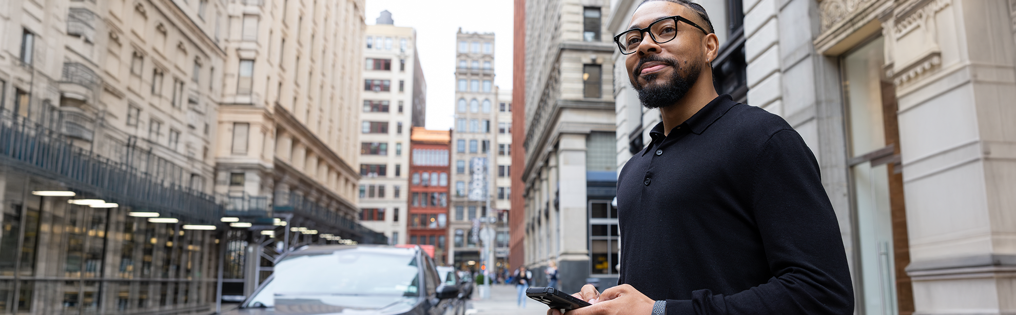 photo of man looking off in the distance smiling. city street and buildings are in the background.
